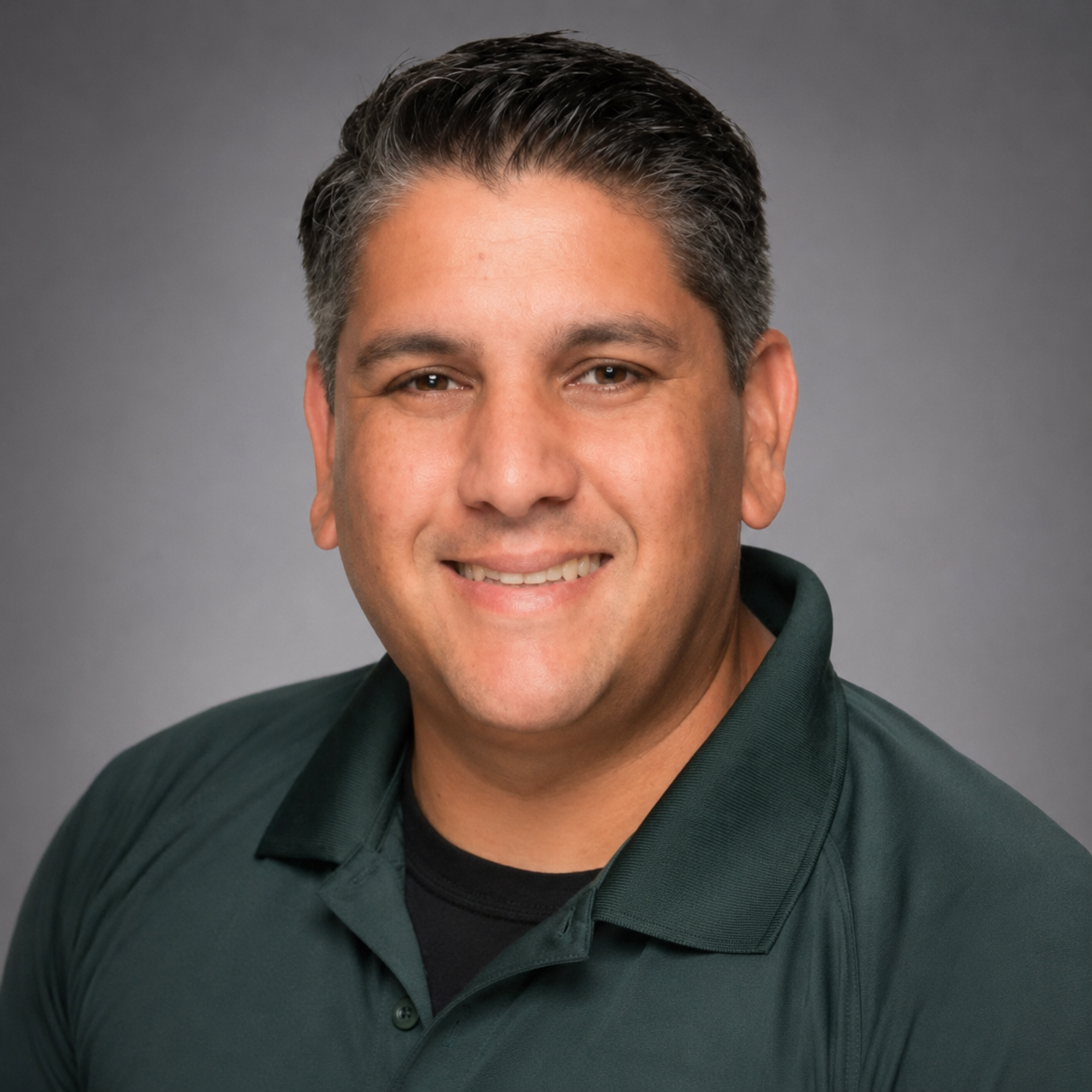 A man with short dark hair is smiling and wearing a green polo shirt.